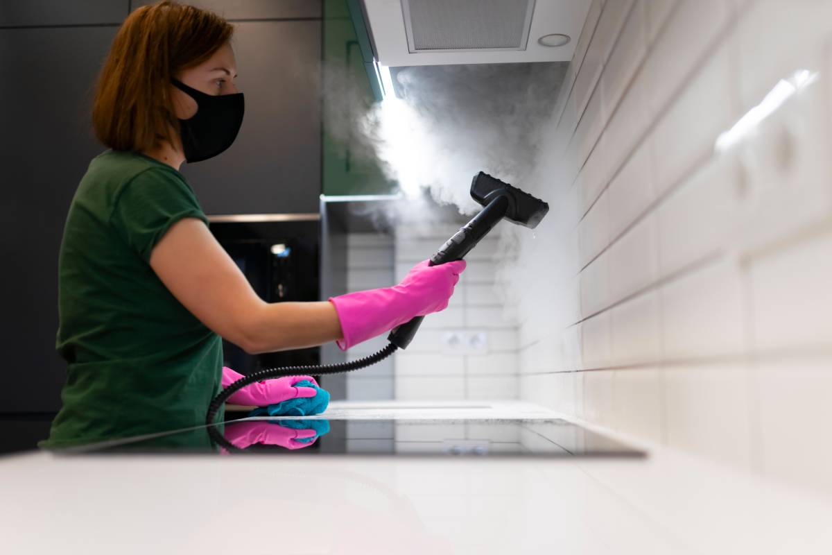 Woman cleaning tiles in the kitchen with steam machine