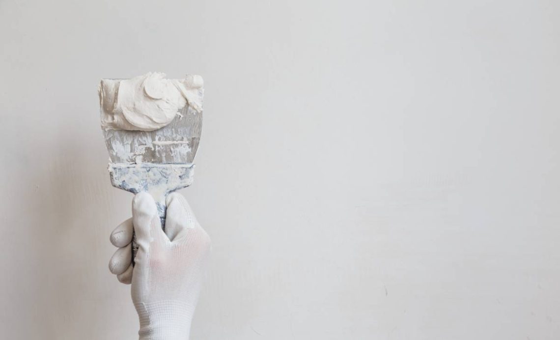 Worker in white gloves performs plastering of the walls of the room