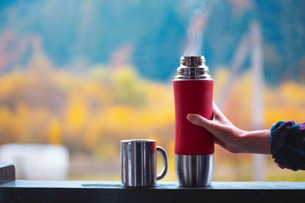 A girl pours tea from a thermos against a background of mountains