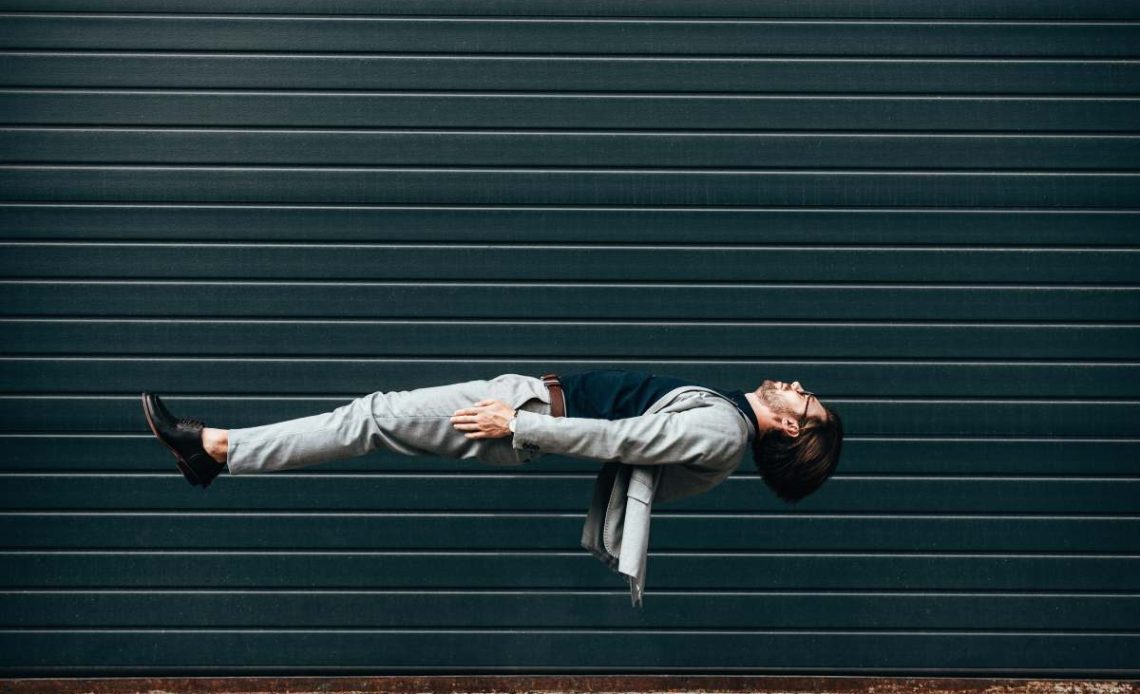 side view of young businessman lying on back in air in front of roller gate