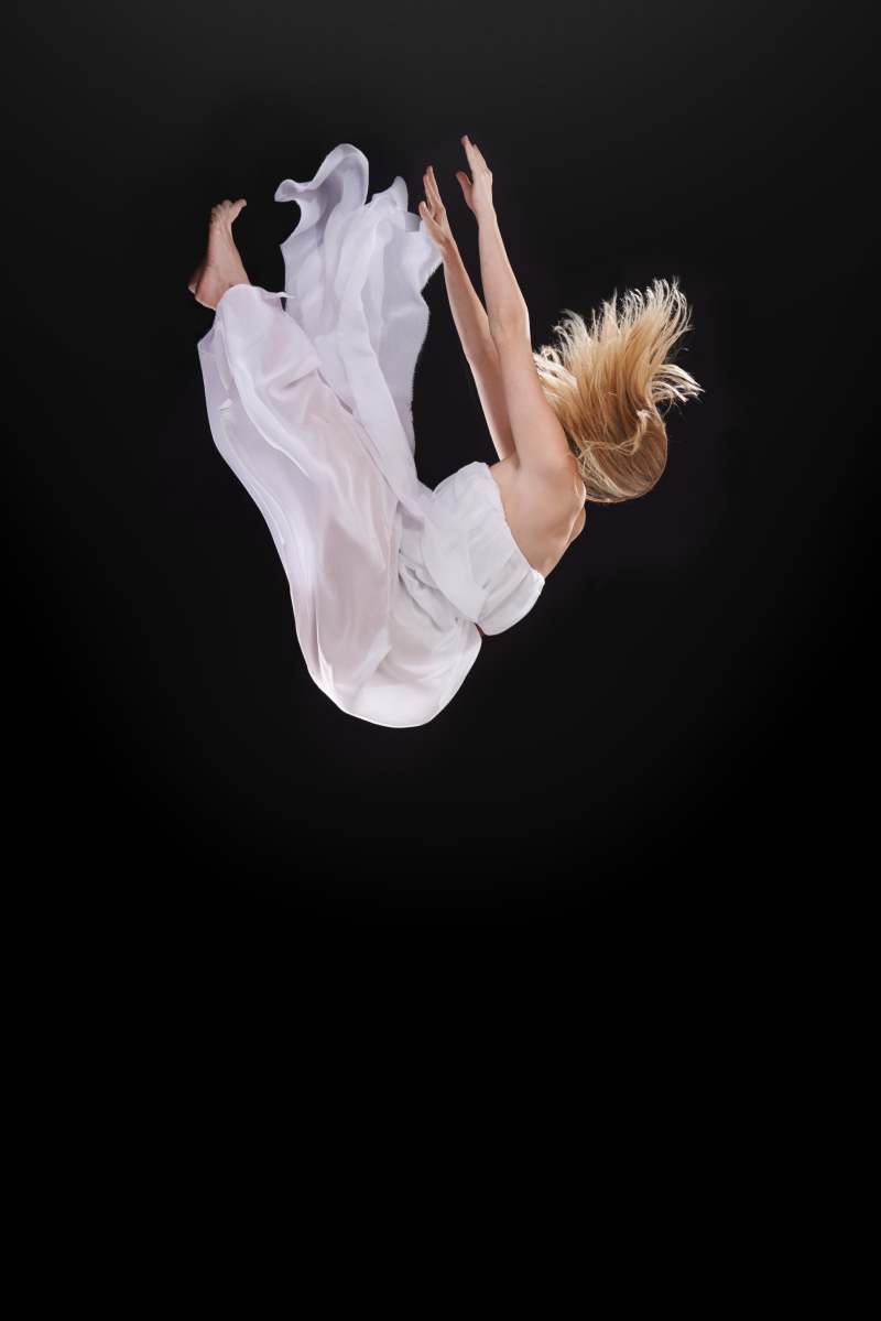 Studio shot of a woman falling upside down against a black background.