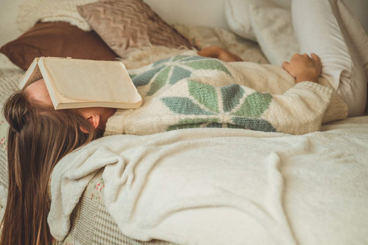 Beautiful young woman sleeping on bed with book covering her face because reading book with preparing exam of college, girl sleepy with tired so that leisure, relax and education concept.