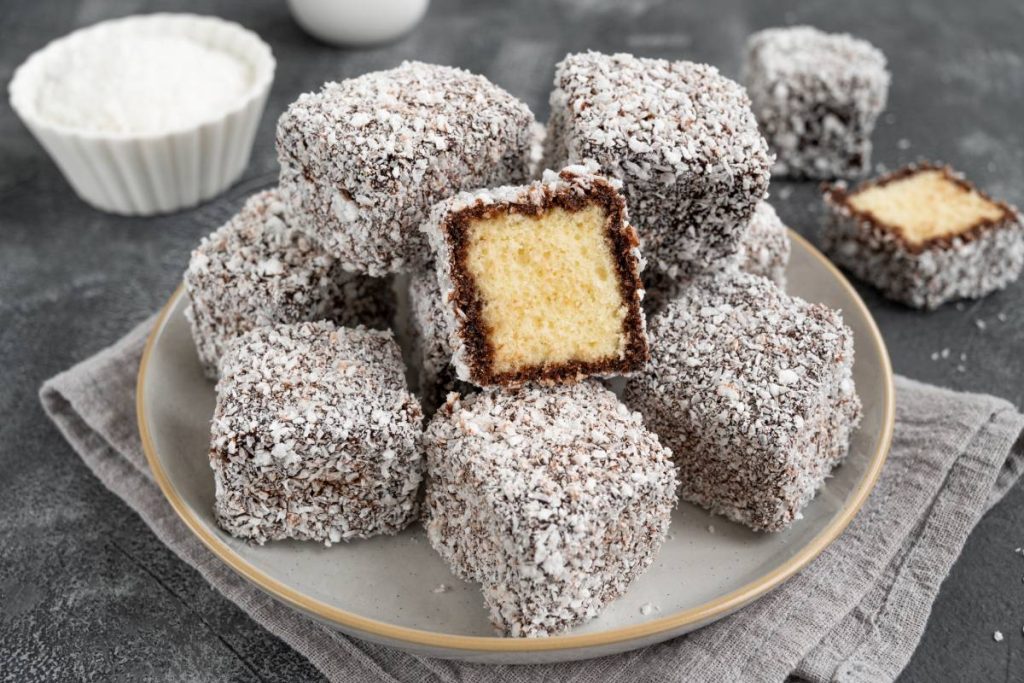 Traditional Australian Lamington cake in chocolate glaze and coconut flakes on a plate on a gray concrete background with a cup of tea. Selective focus